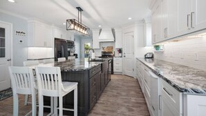 Een moderne keuken met witte kasten, een marmeren eiland en een ingebouwde oven.