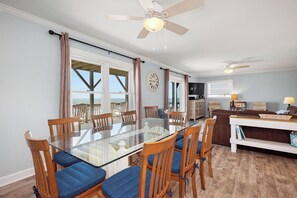 A dining area with a glass table and wooden chairs, a living room with a sofa and TV, and a balcony with a view.
