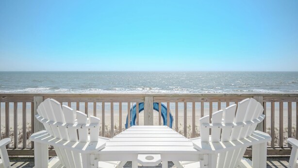 Een houten terras met twee witte Adirondack-stoelen gericht op de oceaan.