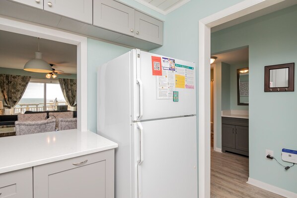 Una cocina con un refrigerador blanco, paredes azul claro y vista a un balcón.
