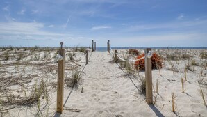 Un sendero arenoso en la playa con postes de madera y barreras de cuerda.