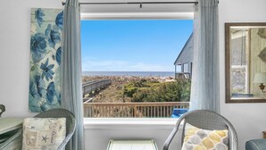 Habitación con vista a la playa y un puente, sillas de mimbre y un cuadro de flores.