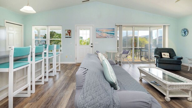 A spacious living room with a large sofa, a coffee table, and a dining area with chairs. - See Otter: Beachwalk cottage in East Beach overlooking the marsh of Davis Canal (Oak Island)