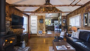 Ein gemütliches Blockhaus-Interieur mit Kamin aus Stein, einer schwarzen Ledersofa und Holzwänden sowie einem Fernseher.