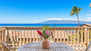 Une terrasse en bois avec une table ronde et des chaises, une clôture en bois et une vue sur l’océan et les montagnes.