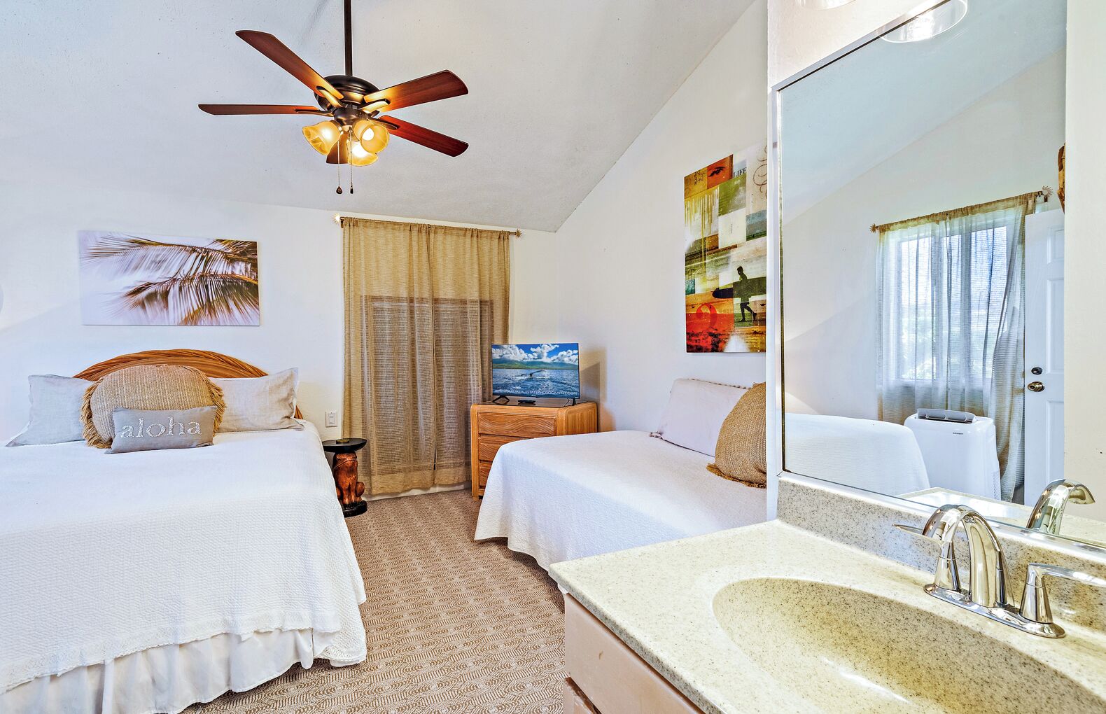 A hotel room with two beds, a ceiling fan, a television, a large mirror, and a bathroom with a sink and toilet.