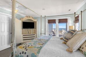 A bedroom with a bed, a television, a wardrobe, and a balcony with a view. - Surviving Stress: Exquisite Oceanfront Caswell Beach Home Perfect for Small Beac (Caswell Beach)