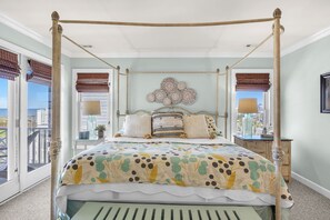Un lit à baldaquin avec une couvre-lit à motifs floraux, une table de chevet avec une lampe et une vue sur la ville à travers de grandes fenêtres.