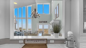 A kitchen with a sign reading "Kitchen Gatherings" and a large window overlooking a deck. - Surviving Stress: Exquisite Oceanfront Caswell Beach Home Perfect for Small Beac (Caswell Beach)