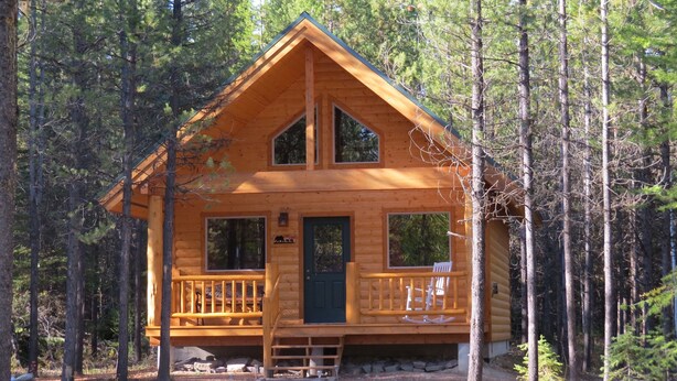 A log cabin with a front porch, two windows, and a door. - A Little Peace of Heaven, Cabin #1 (Polebridge)