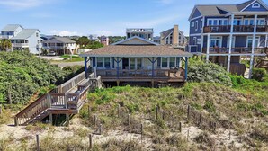 Een vakantiehuis aan het strand met een houten terras, een overdekte veranda en uitzicht op de oceaan.