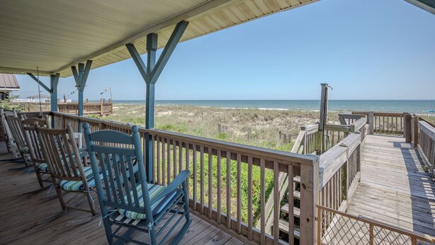 Een overdekt terras met houten stoelen en uitzicht op het strand.