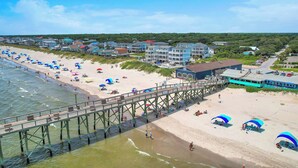 Een strand met een pier, strandparasols en strandhuisjes.