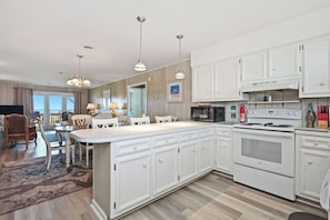 A modern kitchen with white cabinets, a large island, and a built-in oven. - Surfsong: Classic Oceanfront Cottage, Dog-friendly (Oak Island)