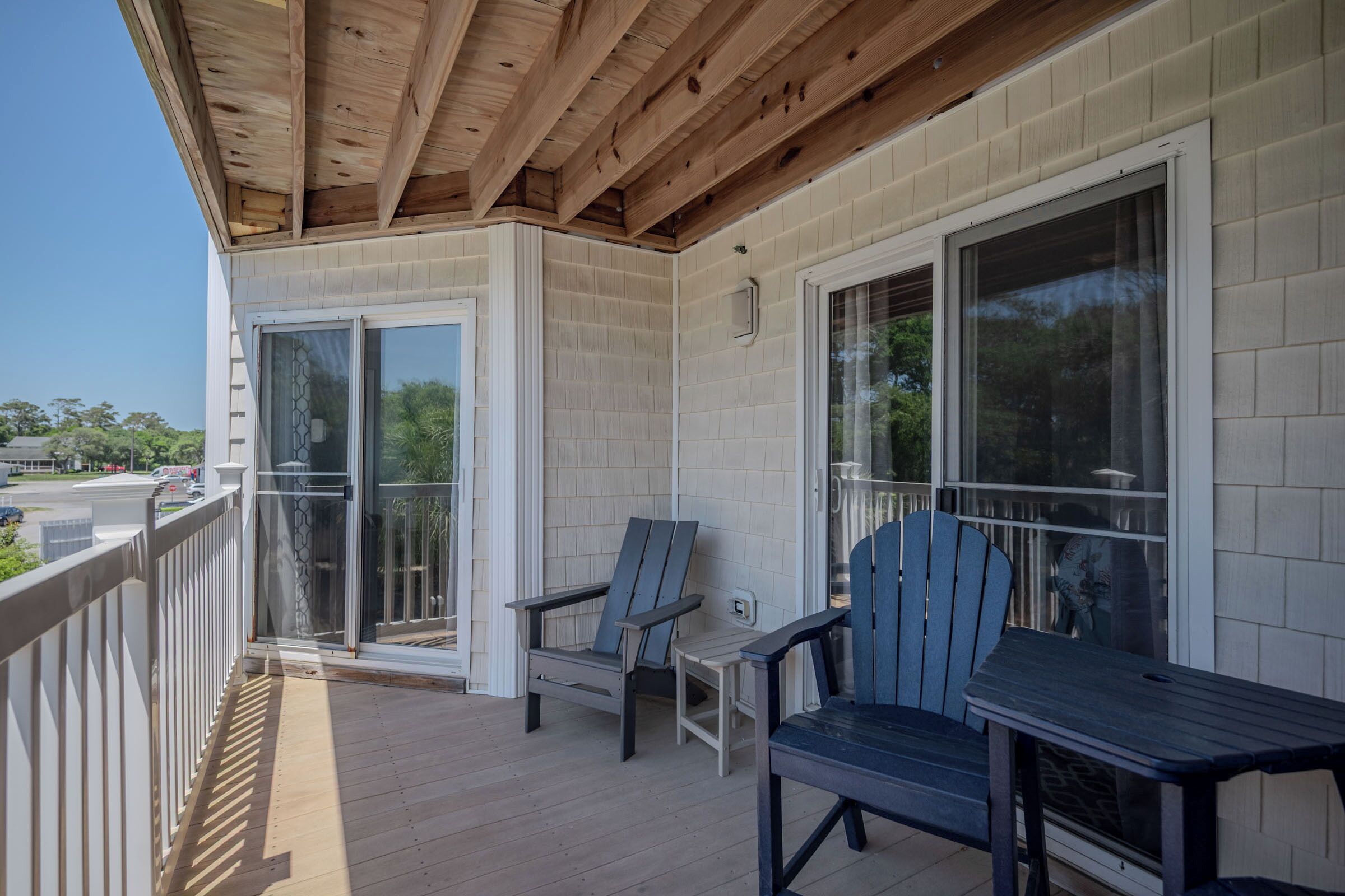 A covered porch with two Adirondack chairs, a wooden deck, and a glass door leading to the interior.