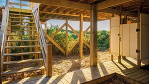 A wooden deck with a wooden ladder leading to a loft area, surrounded by natural vegetation. - Caswell Cabana: Oceanfront, Split Floor Plan, Views of Lighthouse (Caswell Beach)