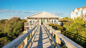 A wooden boardwalk leading to a beach house with a balcony and a view of the beach. - Caswell Cabana: Oceanfront, Split Floor Plan, Views of Lighthouse (Caswell Beach)