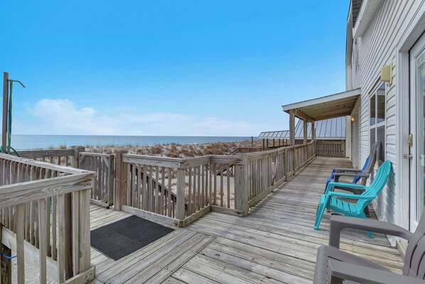 Een houten terras met uitzicht op het strand, een overdekt gedeelte met stoelen en een houten balustrade.