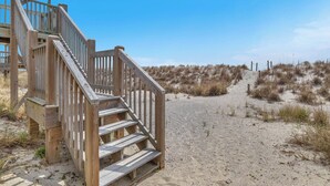 Eine Holztreppe führt zu einem Sandstrand bei blauem Himmel.