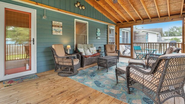 A covered porch with wicker furniture, a ceiling fan, and a view of a house in the background. - Hook Wine and Sinker: Fenced Yard for Dogs, Hot Tub! (Yaupon Beach)