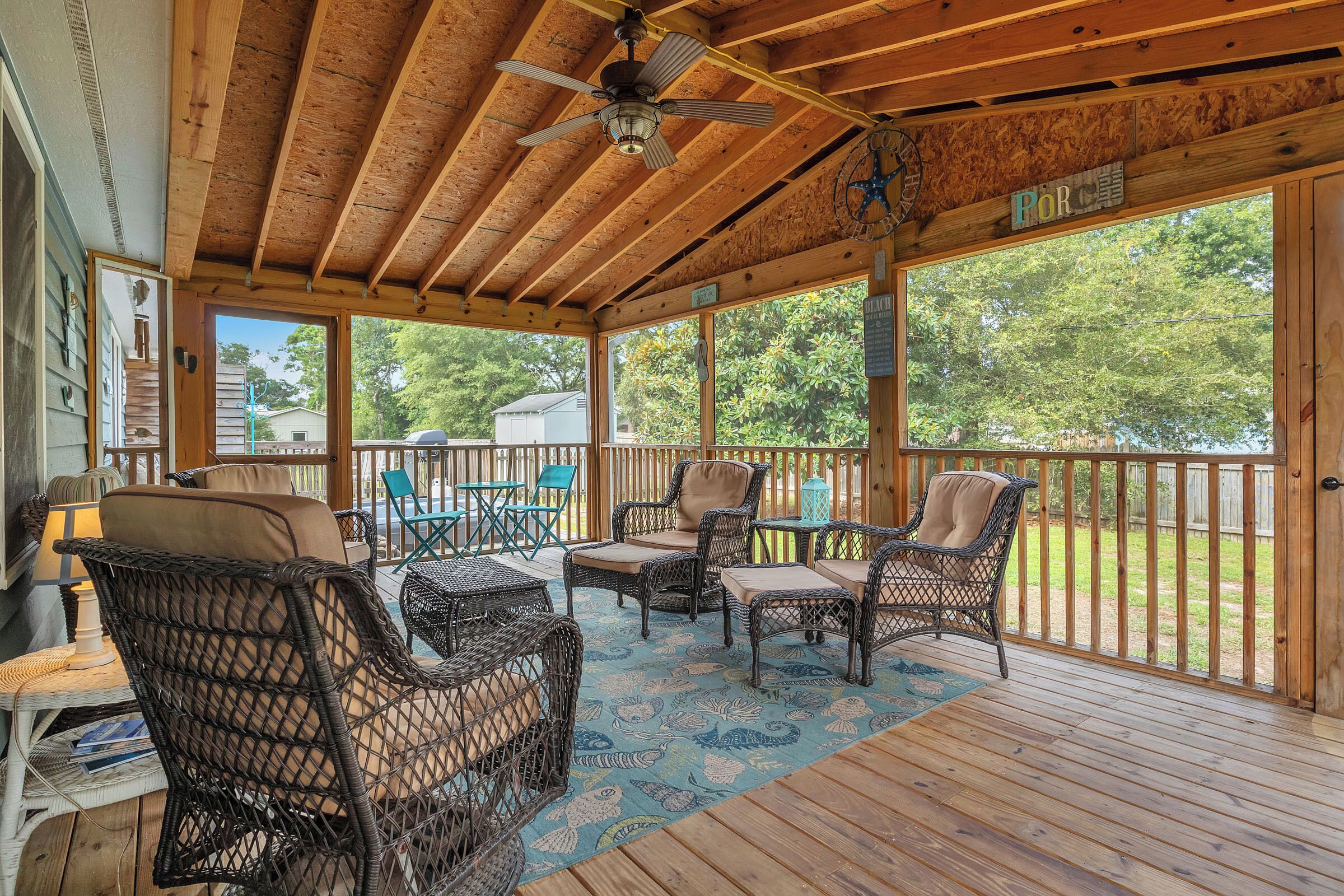 A covered outdoor area with wicker furniture, a ceiling fan, and a view of the backyard.