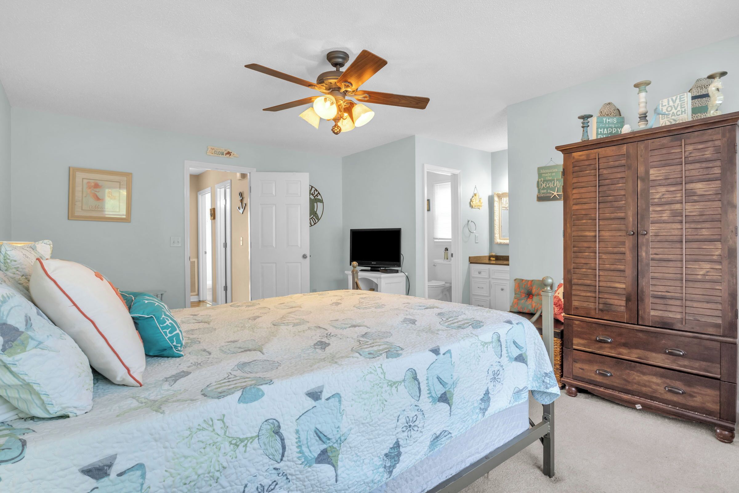 A bedroom with a bed, a ceiling fan, a dresser, and a television.