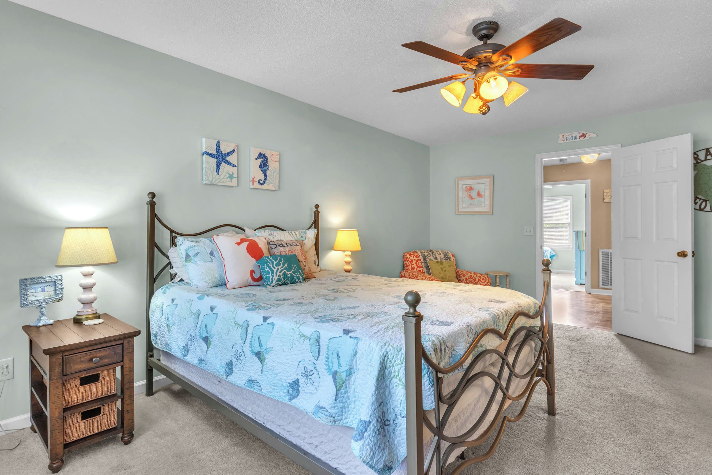 A bedroom with a bed, two bedside tables, a ceiling fan, and a door leading to another room.
