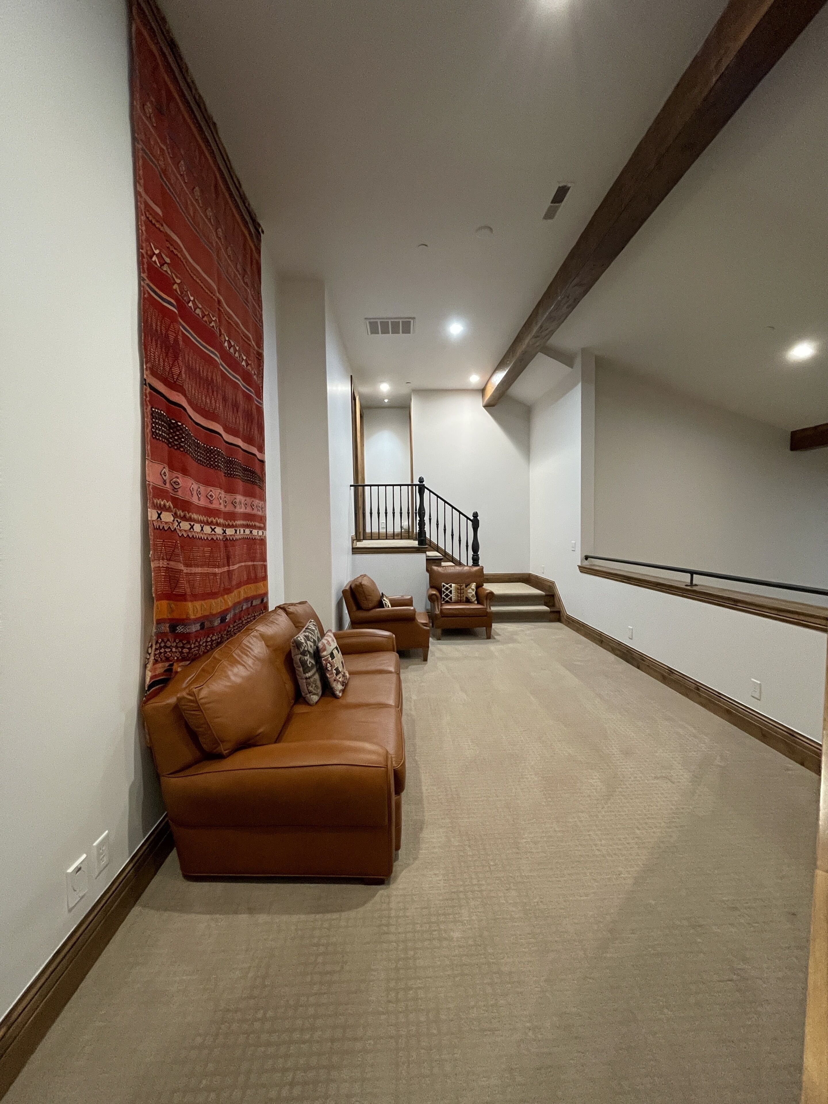 A spacious living area with a brown leather sofa, a patterned rug, and a staircase leading to an upper floor.