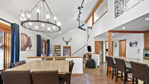 Tilava ruokailutila, jossa on suuri puinen pöytä ja tuolit, moderni kattokruunu ja kattotuuletin.