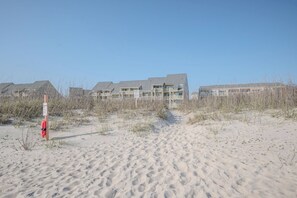 Een strandhotel met meerdere gebouwen, een zandpad dat naar de ingang leidt, en een redderspost.