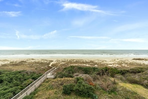 Un paisaje costero con un paseo marítimo de madera que lleva a la playa, rodeado de dunas y vegetación.
