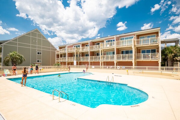 Un hotel con piscina, varios balcones y un edificio grande contiguo al área de la piscina.