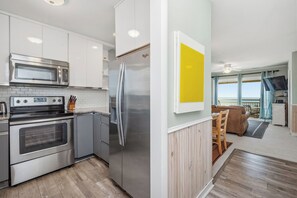 Een moderne keuken met roestvrijstalen apparatuur, een eetgedeelte met uitzicht, en een woonkamer met een bank en een televisie.