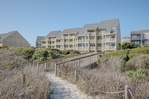 A beachfront residential building with multiple balconies and a sandy pathway leading to the entrance.