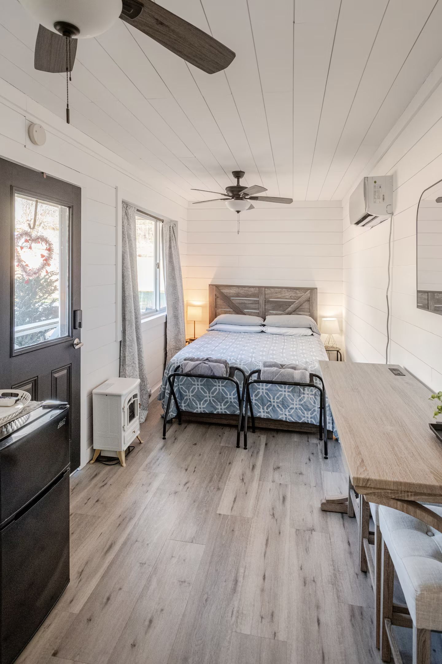 Une chambre à coucher comprenant un lit, des tables de chevet, un bureau, un ventilateur de plafond et une fenêtre avec des rideaux.
