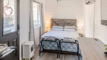 Une chambre à coucher comprenant un lit, des tables de chevet, un bureau, un ventilateur de plafond et une fenêtre avec des rideaux.