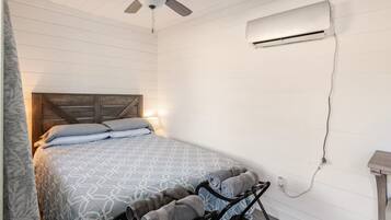 A bedroom with a bed, a ceiling fan, an air conditioning unit, and a bedside table.