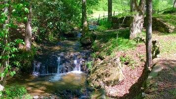 A small waterfall in a forested area with a stone wall and a wooden fence in the background.