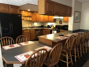 A kitchen with wooden cabinets, a black refrigerator, a dishwasher, and a dining area with wooden chairs and a table. - Peaceful Hocking Hills Vacation Retreat (Rockbridge)