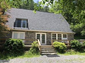 A two-story stone house with a gray shingled roof, a front porch with steps, and a small deck. - Peaceful Hocking Hills Vacation Retreat (Rockbridge)