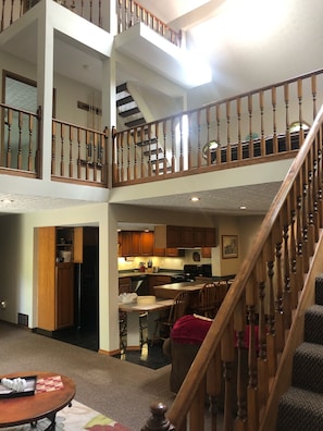 A spacious multi-level home with a central staircase, wooden railings, and a kitchen area. - Peaceful Hocking Hills Vacation Retreat (Rockbridge)