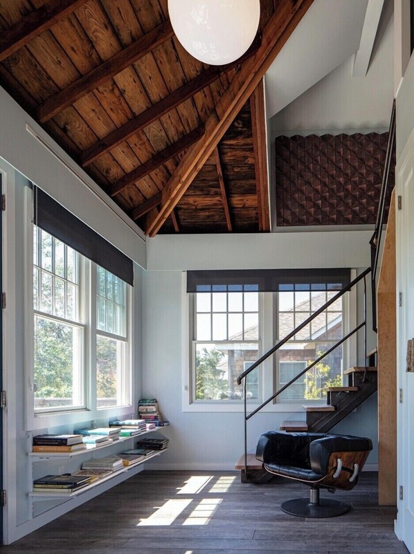 A modern interior with a wooden ceiling, built-in bookshelves, a black leather chair, and a staircase with a black railing.