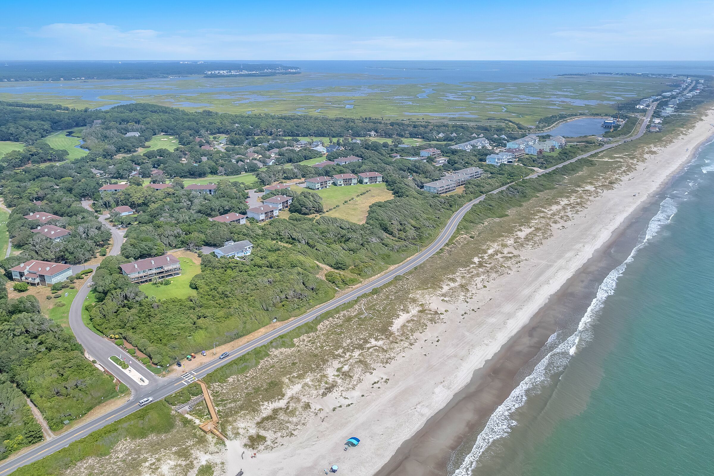 An aerial view of a coastal area with a beach, houses, and a road.