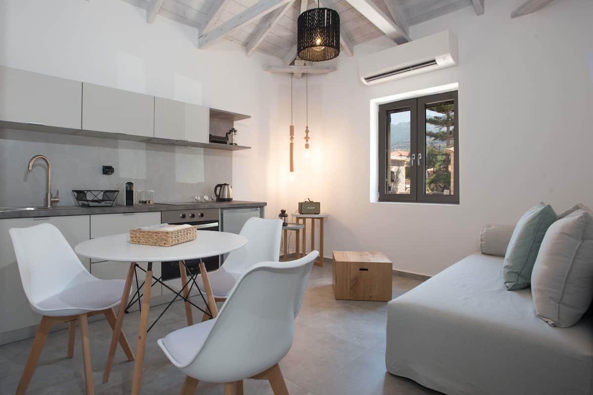 Una cocina moderna con armarios blancos, una mesa de comedor con sillas y un horno empotrado. Se ve una ventana con vistas al exterior.