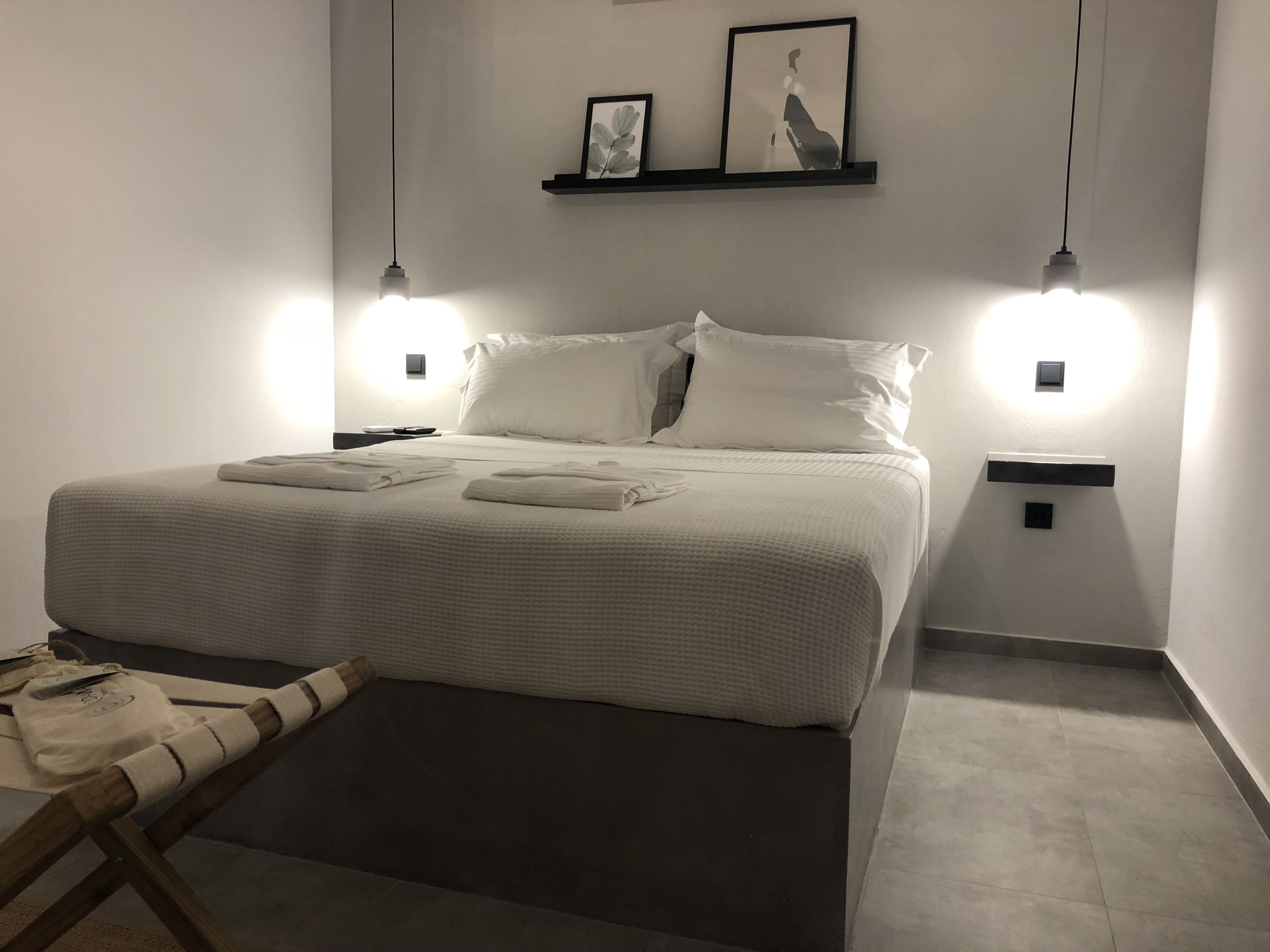 A neatly made bed with white linens and towels, two bedside lamps, and a small shelf with framed pictures above the bed.