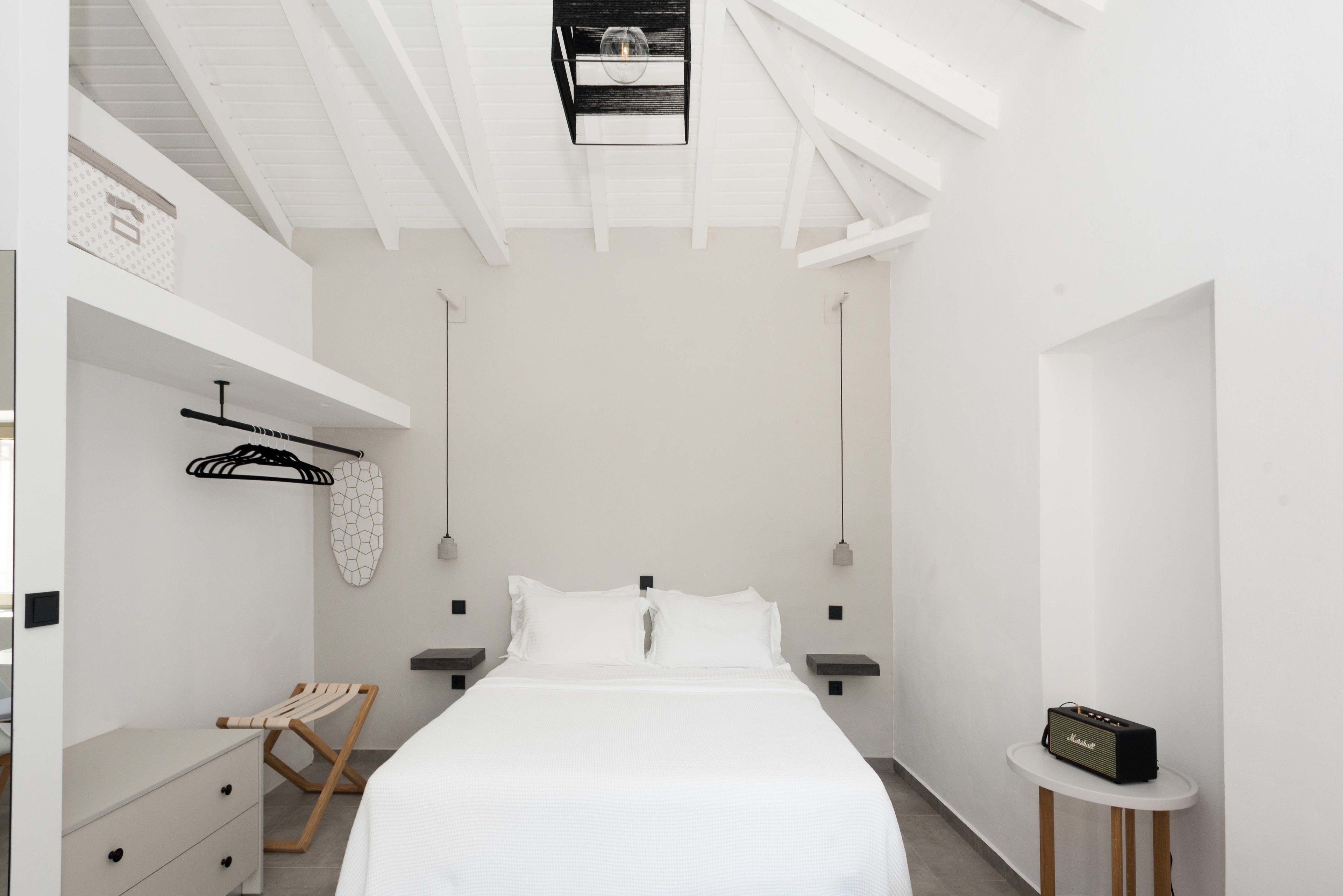 A modern bedroom with a bed, bedside tables, a hanging light fixture, and a small table with a radio.