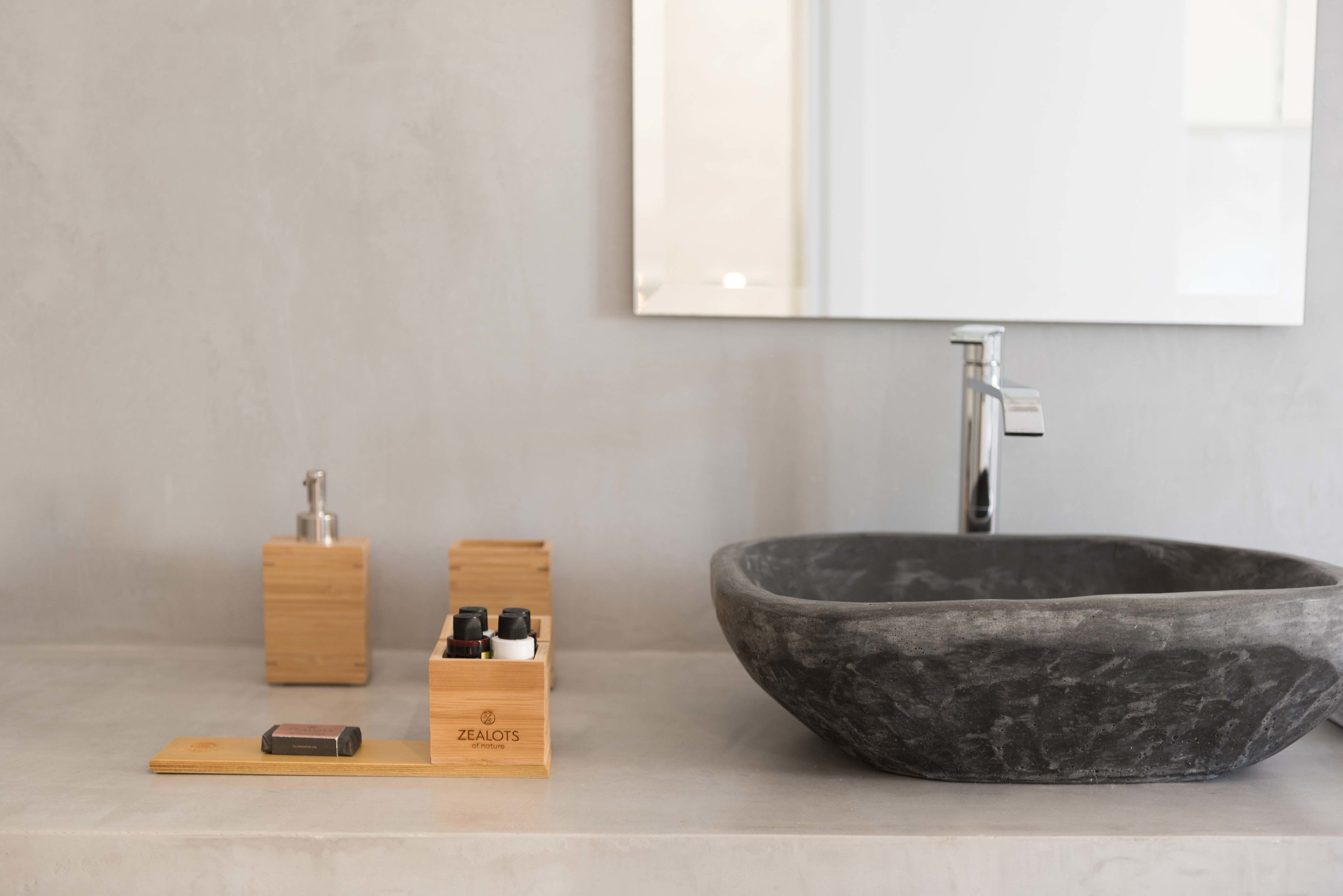 Une salle de bain moderne avec un grand lavabo en pierre sombre, un distributeur de savon en bois et une petite boîte en bois contenant un appareil de recharge.