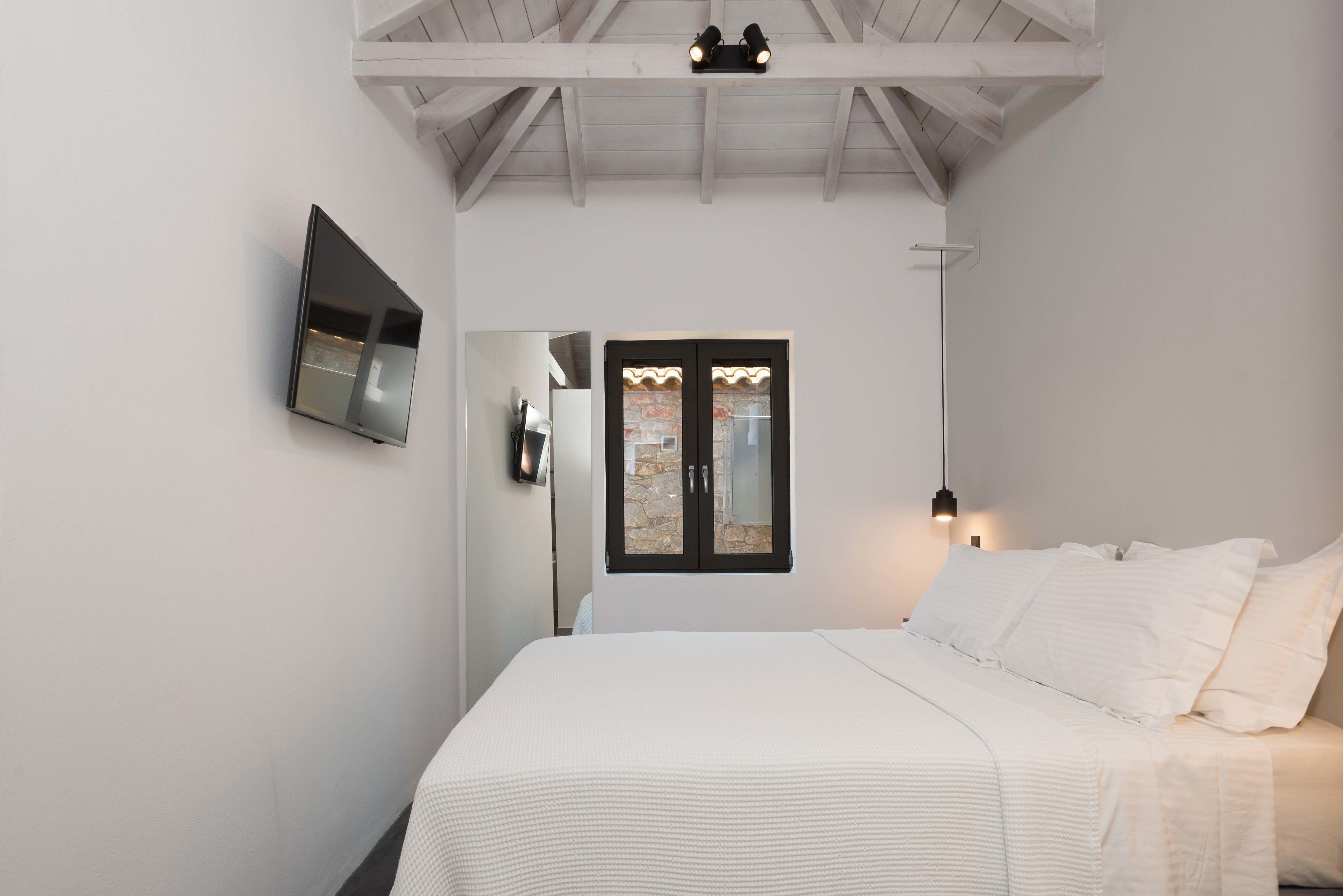 Un dormitorio con una cama, un televisor de pantalla plana montado en la pared, una ventana con muro de piedra y un ventilador de techo.