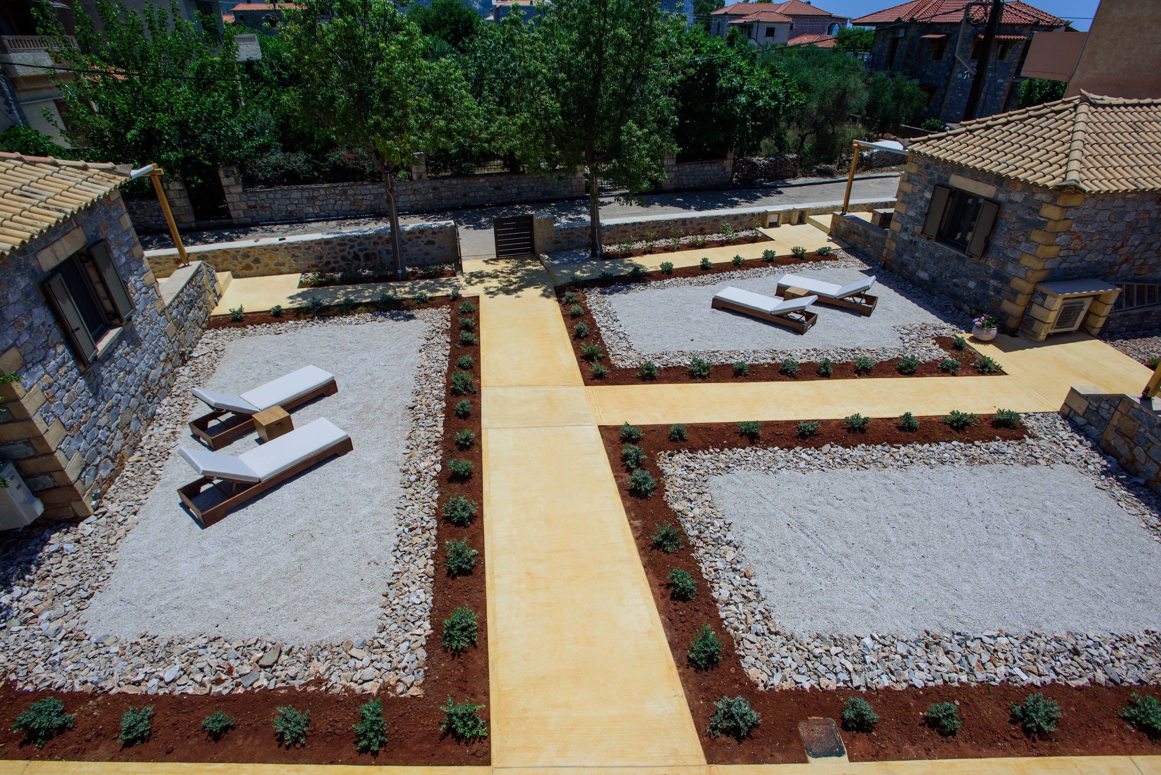 Un patio con edificios de piedra, dos tumbonas y un camino central.