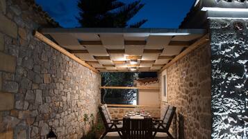 An outdoor patio with stone walls, a wooden pergola, and a table set for dining.